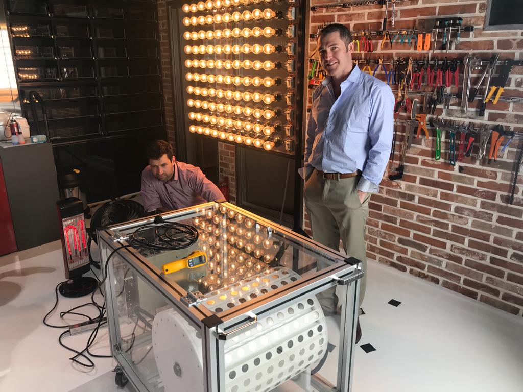 Raven and a colleague with the MG10 prototype powering a full wall of light bulbs — demonstrating real power output